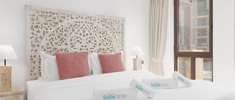 A hotel room with a large bed, white bedding, a decorative headboard, two bedside lamps, and a window with curtains.