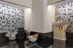 A modern kitchen with black and white diamond-patterned backsplash, a coffee machine, a bowl of snacks, and utensils in a holder. - Experience Opulent Living at Paramount Midtown (Dubai)