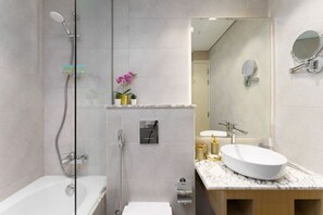 Een moderne badkamer met een douchecabine van glas, een witte badkuip en een marmeren wastafelmeubel met twee wasbakken.