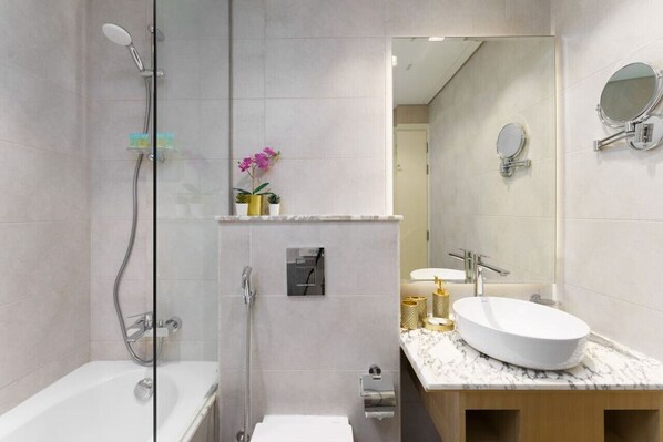 A modern bathroom with a glass-enclosed shower, a white bathtub, and a marble vanity with two sinks.