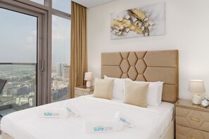 Une chambre d’hôtel avec un grand lit, une vue sur la ville, une tête de lit moderne et un tableau abstrait décoratif.