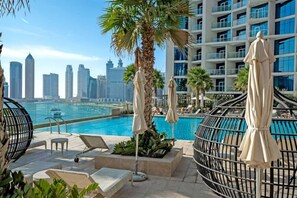 A rooftop pool area with lounge chairs, umbrellas, and a city skyline view. - Your Dream Home in Damac Maison Prive by Suiteable (Dubai)