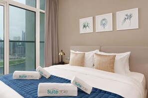 A hotel room with a large bed, a nightstand with a lamp, and three framed botanical prints on the wall. - Your Dream Home in Damac Maison Prive by Suiteable (Dubai)