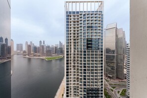 A high-rise building with a grid-like facade, a river in the foreground, and other modern buildings in the background. - Your Dream Home in Damac Maison Prive by Suiteable (Dubai)