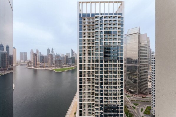 Un edificio de gran altura con fachada enrejada, un río en primer plano y otros edificios modernos al fondo.