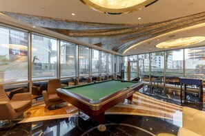 Relax in a spacious area with a pool table and comfortable seating, surrounded by city views and unique ceiling details.