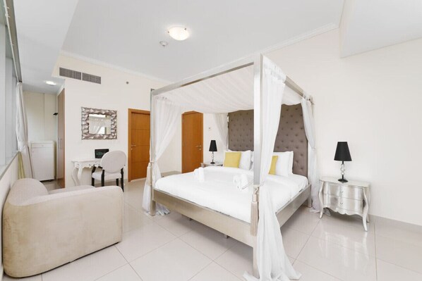 A spacious bedroom with a four-poster bed, a sitting area, a vanity, and a small table with a lamp.