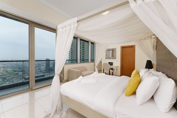 A bedroom with a large bed, a view of the city, and a balcony.