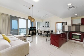 A modern living room with a sofa, a dining area with chairs, a kitchen with red cabinets, and a large window with curtains.