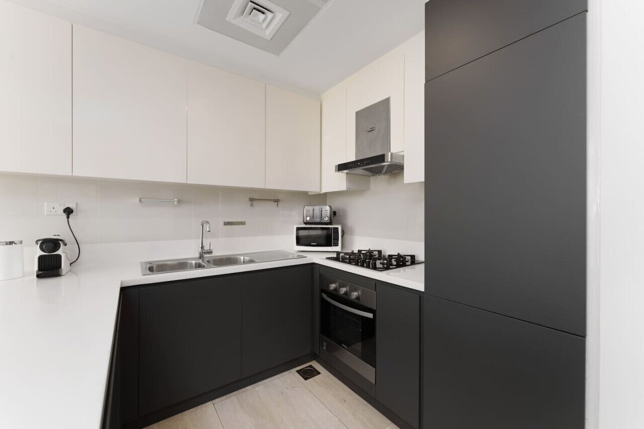 A modern kitchen with white cabinets, a black countertop, a microwave, a toaster, and a stove.