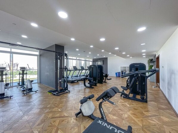 A gym with various exercise equipment, large windows, and a wooden floor.