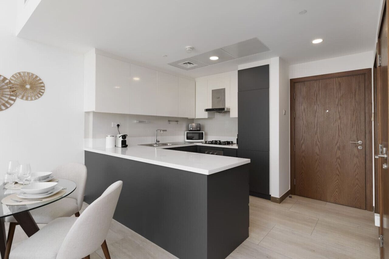 Una cocina moderna con armarios blancos, una isla central y una zona de comedor con mesa y sillas de vidrio.
