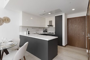 Une cuisine moderne avec des meubles blancs, un îlot central et un coin repas comprenant une table et des chaises en verre.