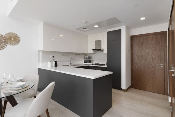 Una cocina moderna con armarios blancos, una isla central y una zona de comedor con mesa y sillas de vidrio.