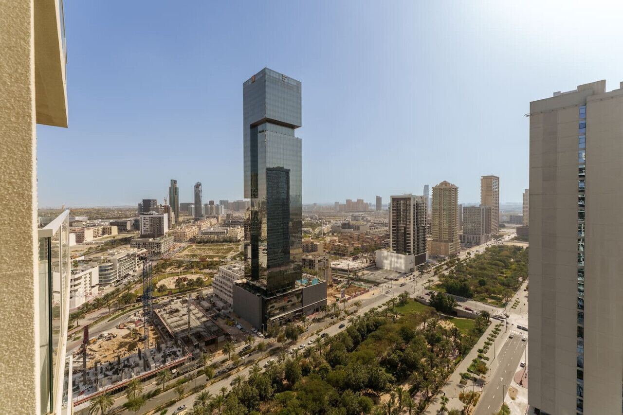 Een hoog gebouw met een moderne glazen gevel, omringd door andere hoogbouw en een mix van stedelijke en groene ruimtes.