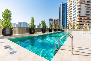 Piscina en la azotea con vistas despejadas del horizonte urbano, rodeada de plantas en macetas y un puesto de socorrista.