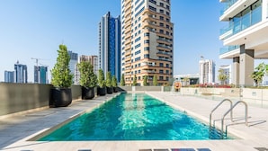 Una piscina en la azotea con agua azul cristalina, rodeada de edificios modernos y plantas en macetas.