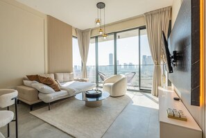 Una habitación de hotel moderna con un ventanal grande, un sofá, una mesita de centro y un televisor en la pared.