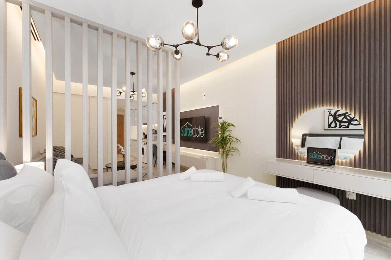 Una habitación de hotel moderna con una cama grande, un televisor, un espejo y una mesita de noche.