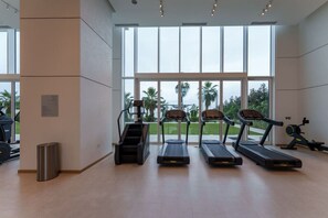 Une salle de sport équipée de tapis de course, d’un appareil de marche en escalier et d’un vélo d’appartement, avec de grandes fenêtres et une vue sur les palmiers.