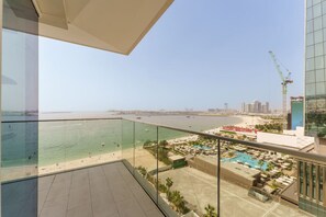 Un balcon avec vue sur une plage, une piscine et une grue de construction au loin.
