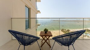 A balcony with two blue chairs, a small table with a plant, and a view of the sea and beach. - Beachfront Luxury Living at La Vie Residence JBR (Dubai)
