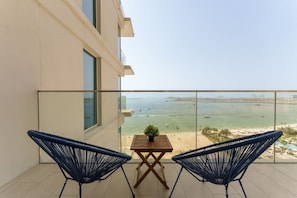 Un balcon avec deux chaises bleues, une petite table ornée d’une plante, et une vue sur la mer et la plage.