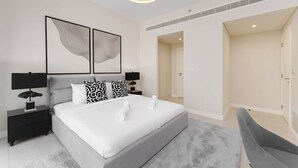 A modern bedroom with a large bed, two bedside tables with lamps, a grey upholstered chair, and abstract wall art. - Beachfront Luxury Living at La Vie Residence JBR (Dubai)