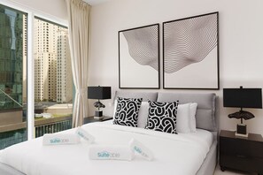 A hotel room with a large bed, two bedside tables, a window with a view of buildings, and two wall-mounted artworks.