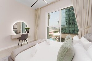 Une chambre d’hôtel moderne dotée d’un grand lit, d’un bureau avec une chaise, d’un miroir rond et offrant une vue sur le paysage urbain par une grande fenêtre.
