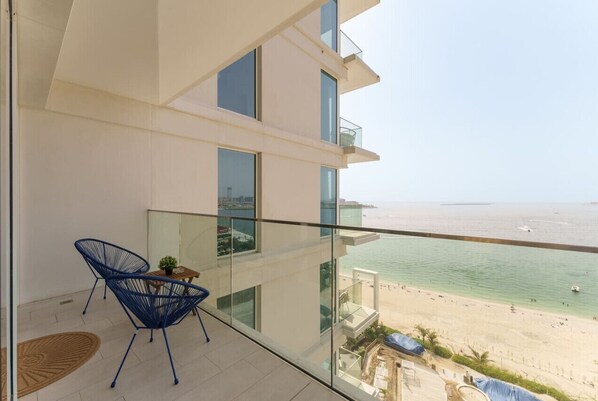 A balcony with a view of the beach, a glass railing, and a blue chair.