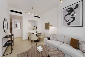 A modern living room with a white sofa, a coffee table, and a dining area with chairs and a table. - Experience Serenity at Binghatti Crest in JVC (Dubai)