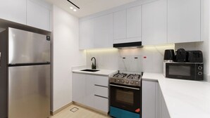 A modern kitchen with white cabinets, a stainless steel refrigerator, a gas stove, an oven, and a microwave.