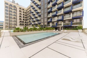 Um edifício de apartamentos moderno com área de piscina no terraço, incluindo espreguiçadeiras e uma piscina.