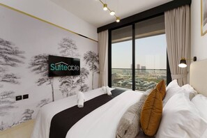 A hotel room with a bed, a TV mounted on the wall, and a large window offering a city view. - Experience Serenity at Binghatti Crest in JVC (Dubai)