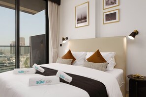 Habitación de hotel con una cama grande, ropa de cama blanca, almohadas marrones y vistas a la ciudad a través de ventanales de piso a techo.