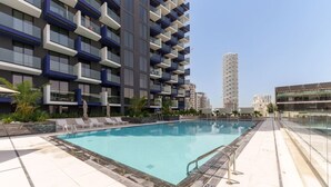A modern building with a swimming pool, lounge chairs, and a clear sky.