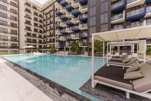 Un hotel moderno con piscina, tumbonas y una zona de estar cubierta.