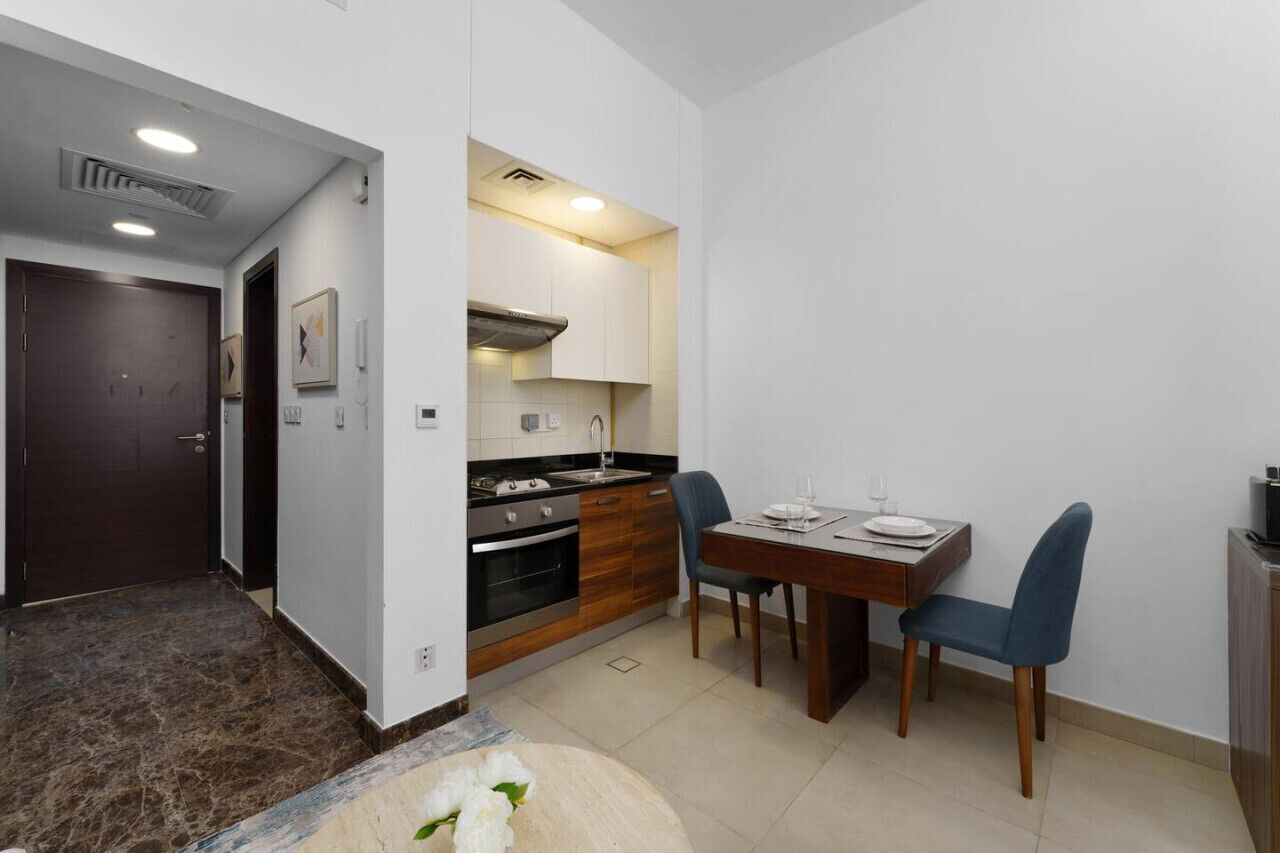 Une cuisine compacte dotée d’appareils électroménagers modernes, une table à manger avec des chaises et une porte donnant sur une autre pièce.