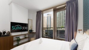 Una habitación de hotel moderna con una cama grande, un televisor de pantalla plana, un escritorio con computadora y vistas a edificios altos.