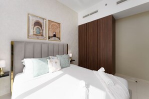 A neatly made bed with a grey headboard, white linens, and decorative pillows. There are two framed pictures on the wall above the bed. - Contemporary Apartment with Burj Khalifa View (Dubai)