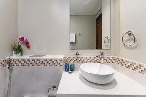 A bathroom with a white sink, a mirror, and a shower. There are decorative plants and toiletries on the counter.