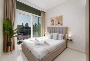 A modern hotel room with a large bed, a city view, a potted plant, and a nightstand with a lamp.