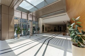 Experience the hotel's elegant lobby, featuring a high ceiling, unique central column, lush greenery, and a well-designed pathway.