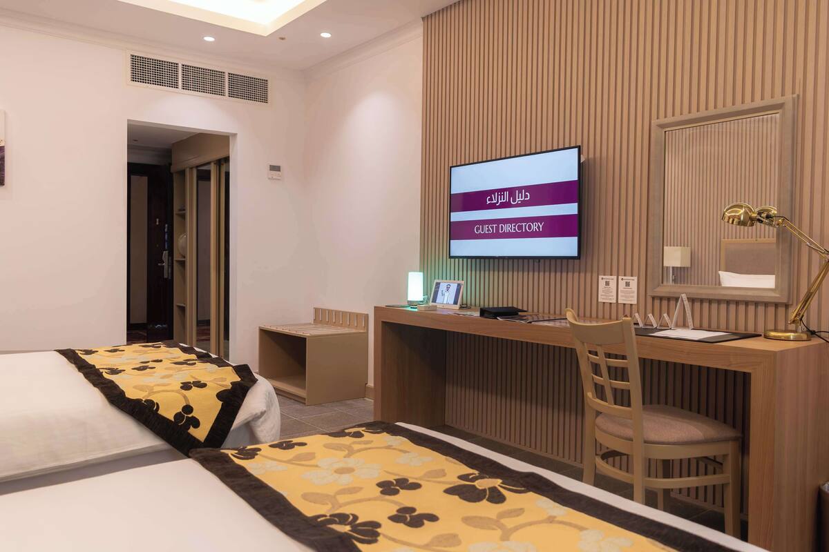 A hotel room with two beds, a desk, a chair, a TV screen displaying 'GUEST DIRECTORY', and a mirror.