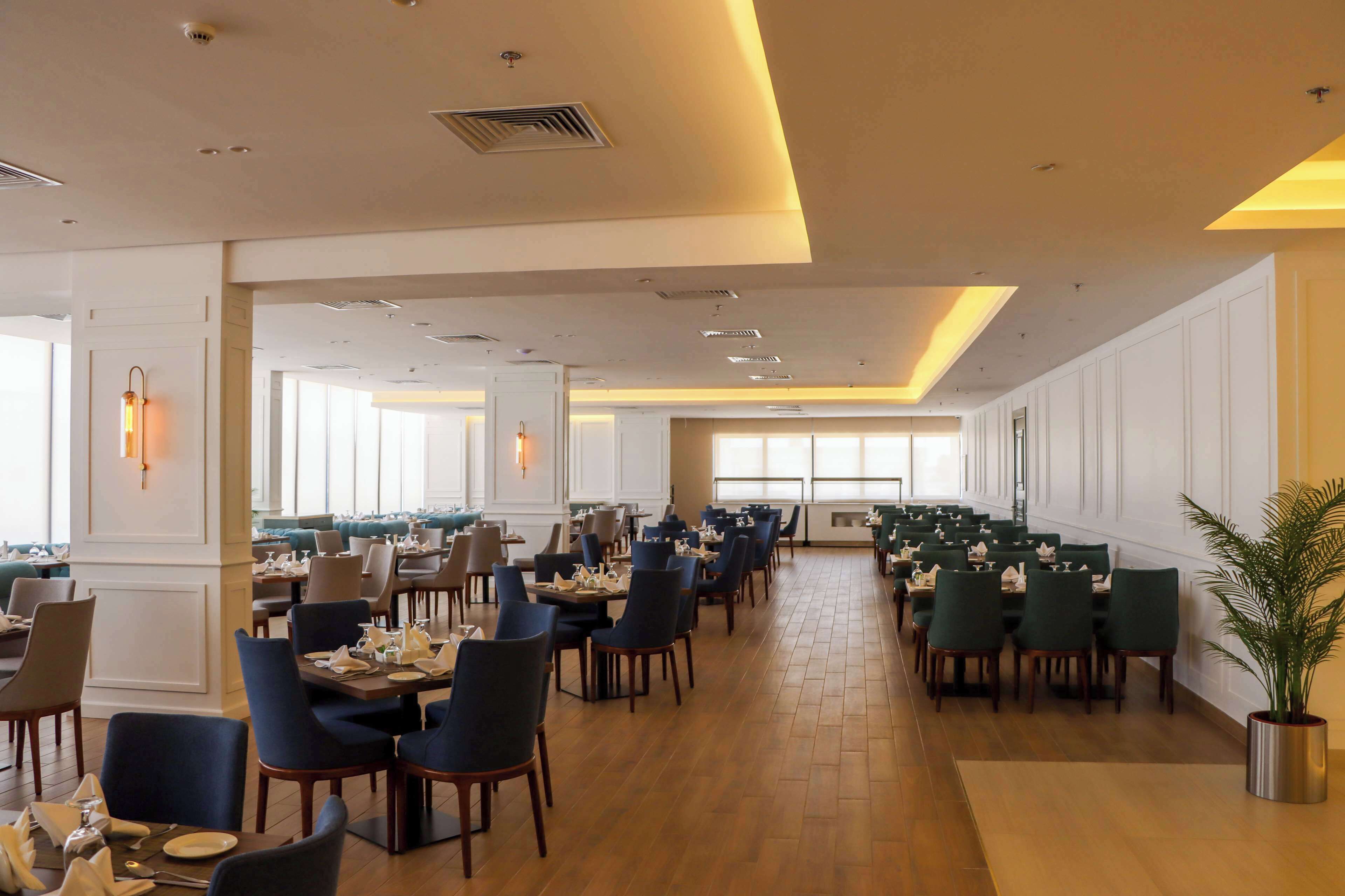 Un vaste espace dédié à la salle à manger, avec de nombreuses tables et chaises, de grandes fenêtres laissant entrer la lumière naturelle et un design moderne au niveau du plafond.