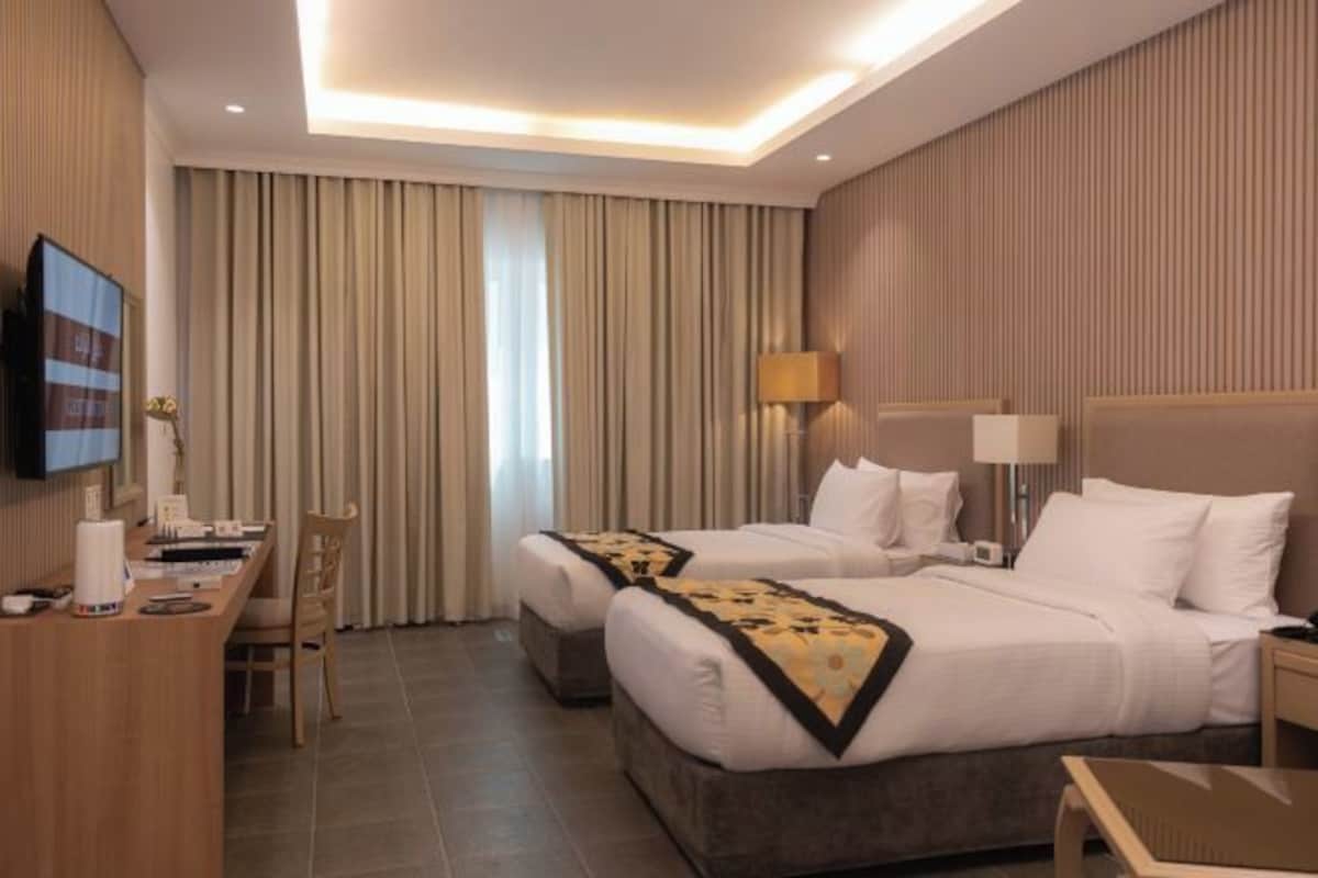 A hotel room with two beds, a desk, a chair, and a TV.