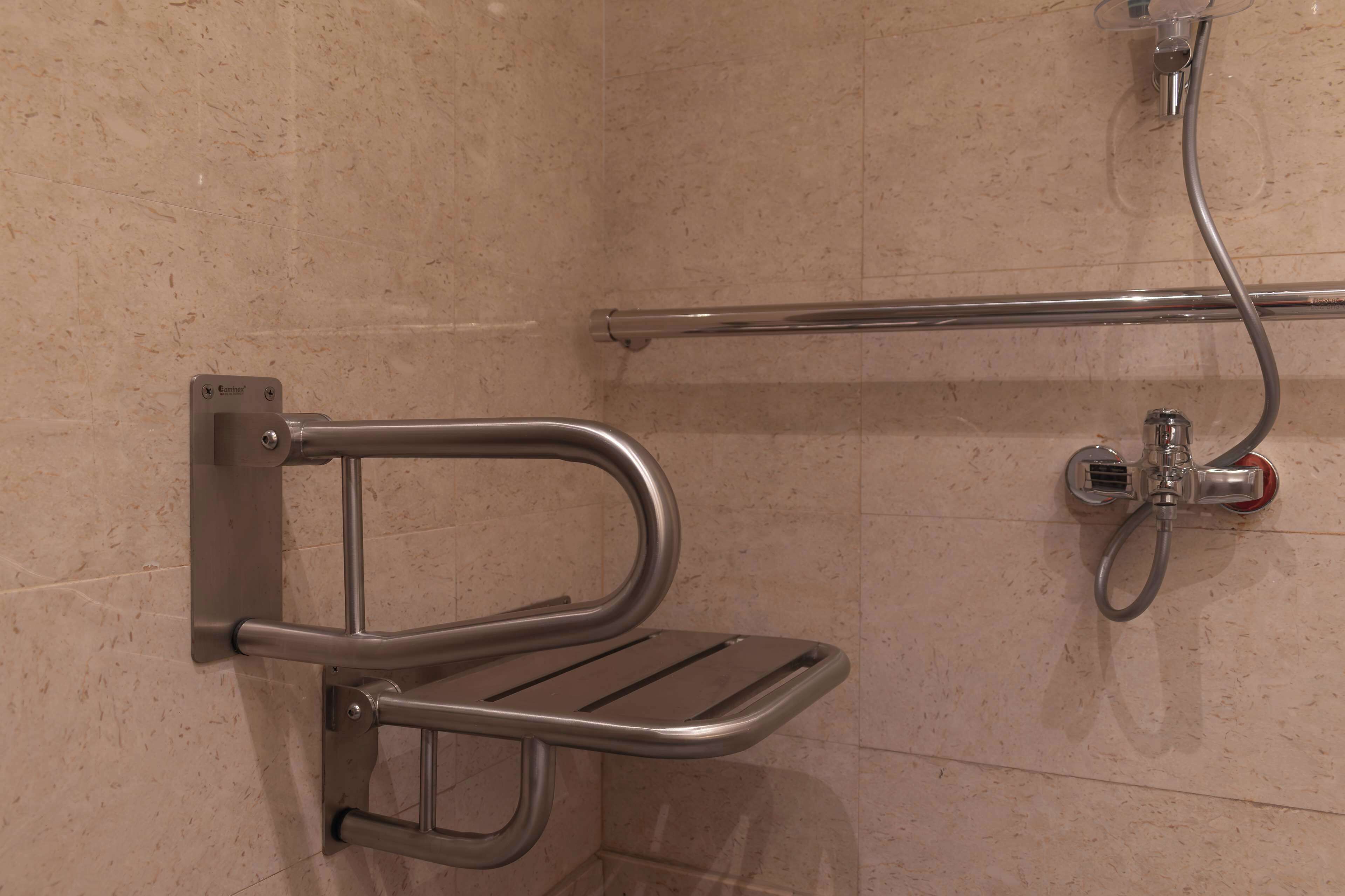 A shower area with a grab bar, a handheld showerhead, and a towel rack.
