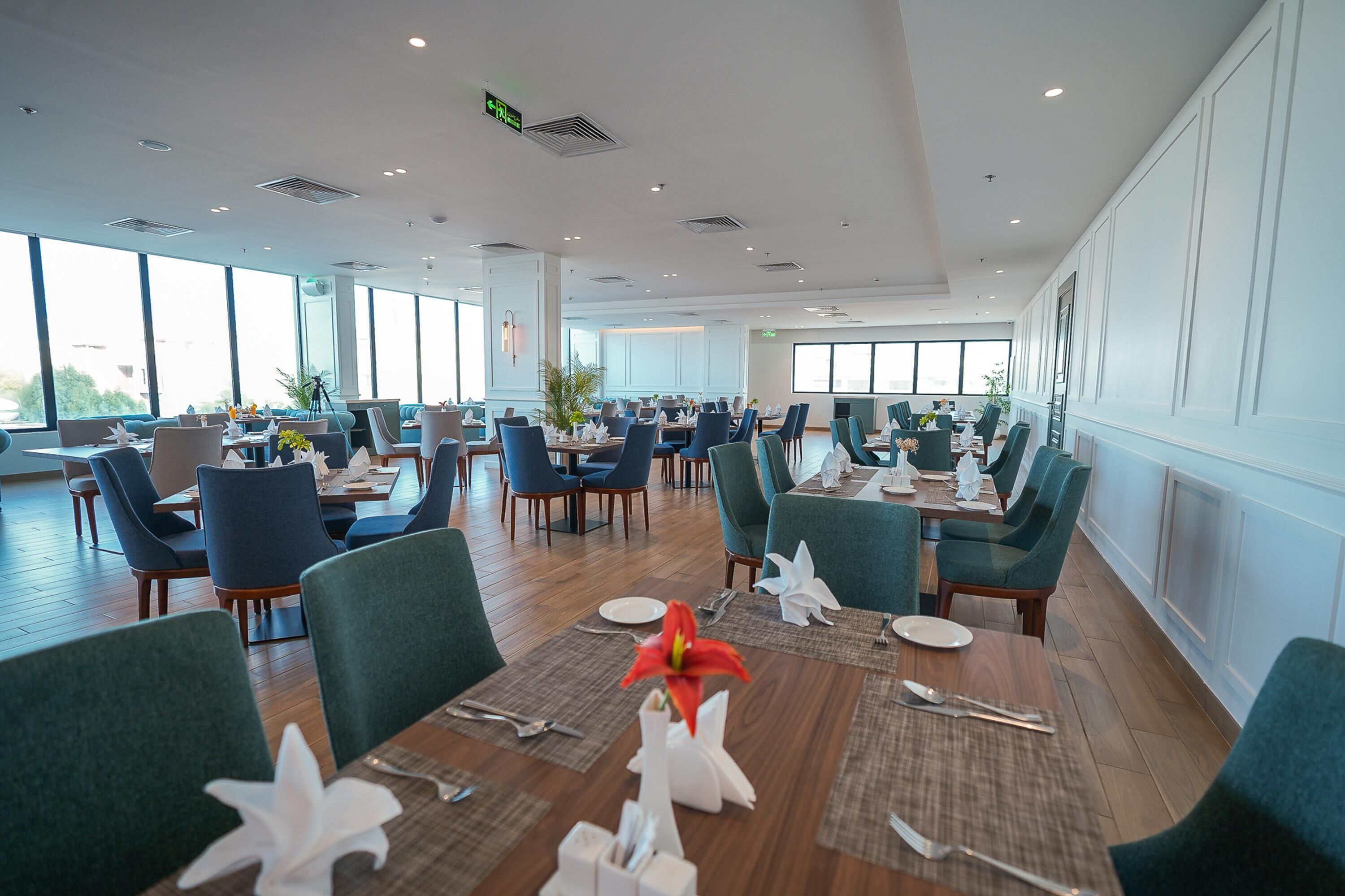 A spacious dining area with multiple tables and chairs, large windows, and a modern interior design.