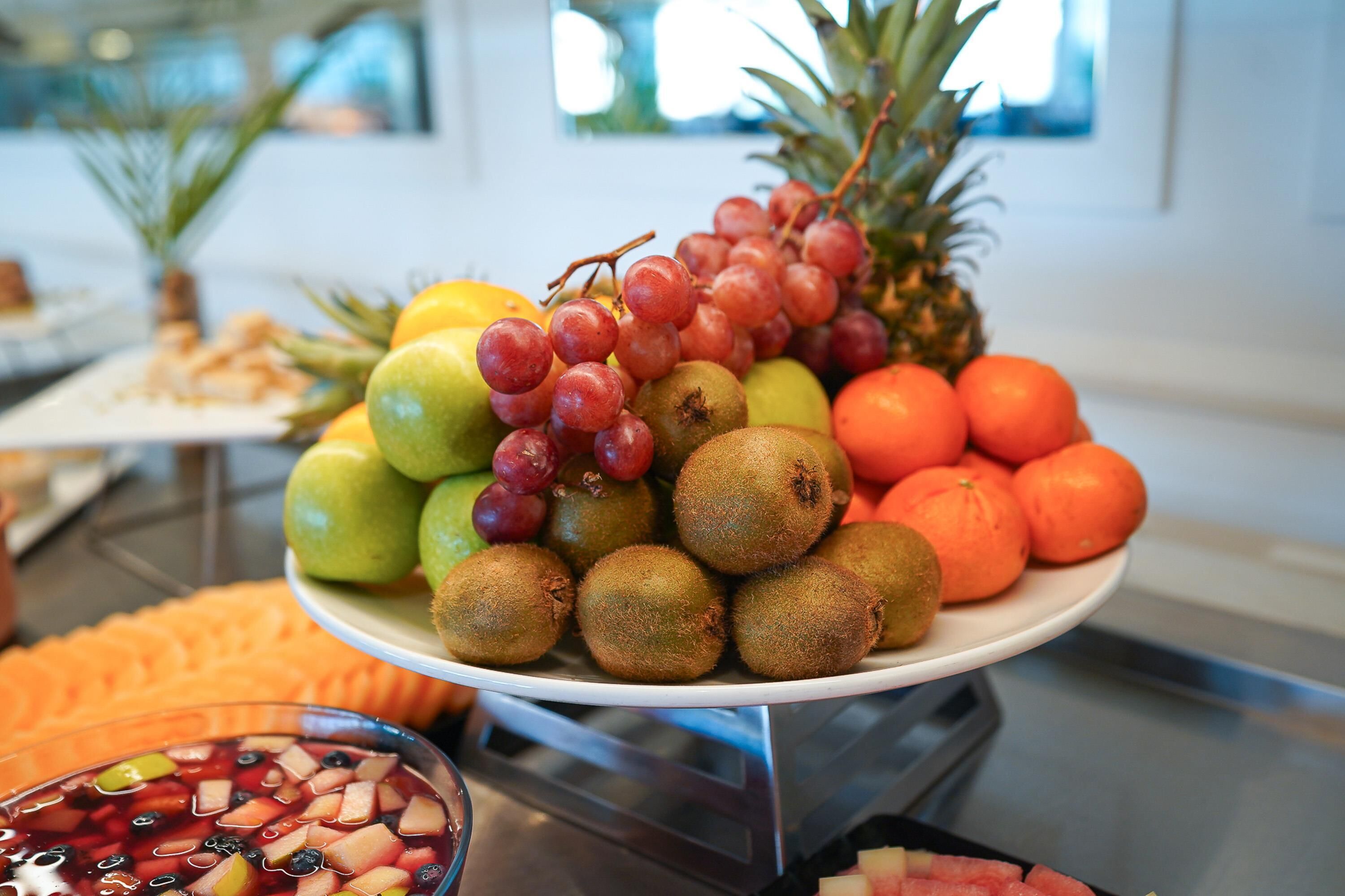 Een fruitschaal met appels, druiven, kippen, sinaasappels en een ananas.